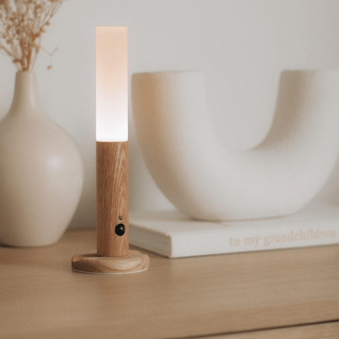 Wooden lamp with a white shade on a wooden surface with decorative items in the background.